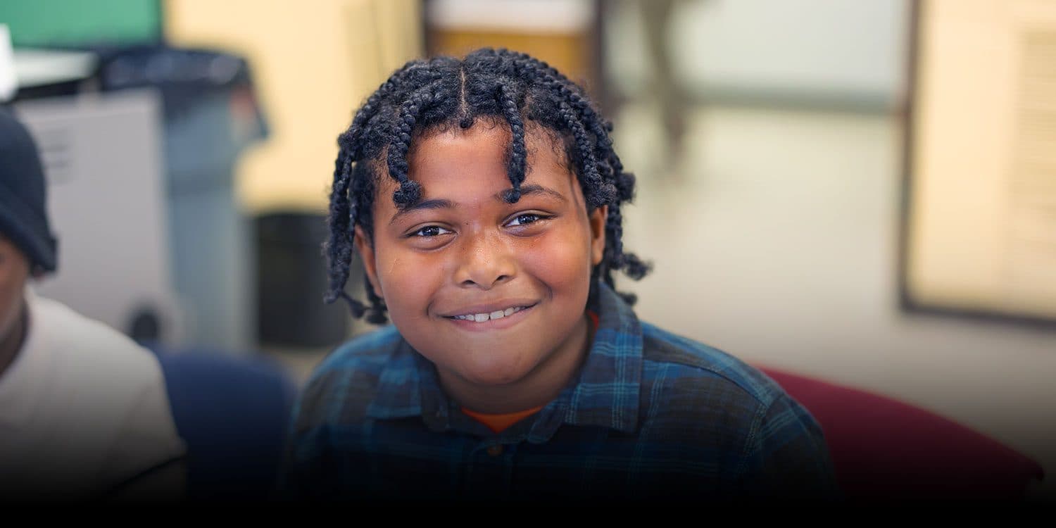 Smiling student with braided hair in a classroom.