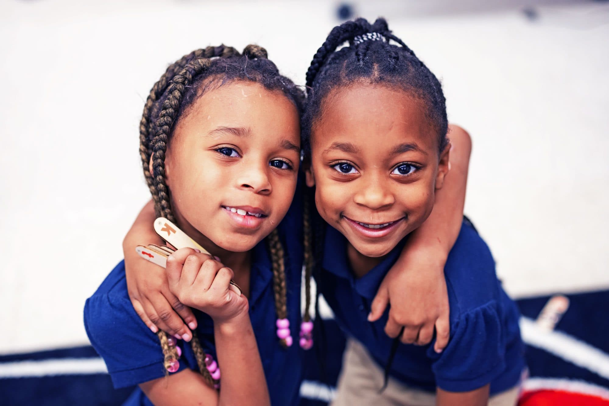 Two smiling students in blue shirts, one hugging the other.