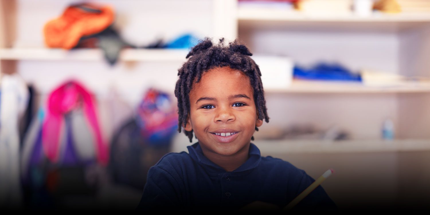 Smiling student holding a pencil in a classroom.