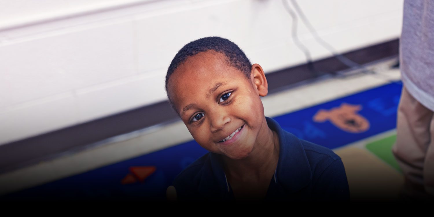 Smiling student sitting on a colorful classroom rug.